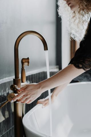 Elegant bathroom scene with a focus on gold faucet and female hands adjusting water flow.